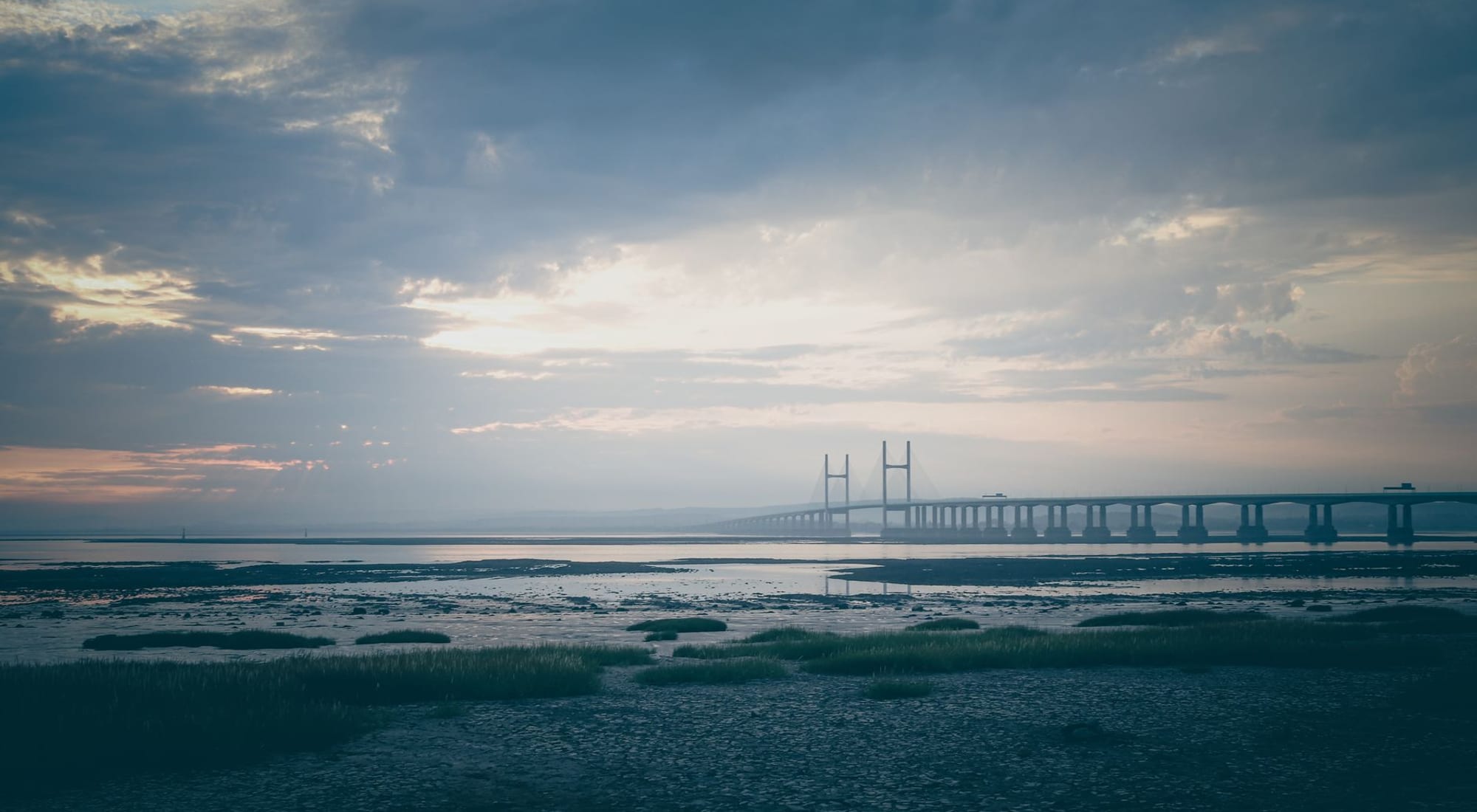 A long bridge reaching across calm water in soft daylight, connecting two shores